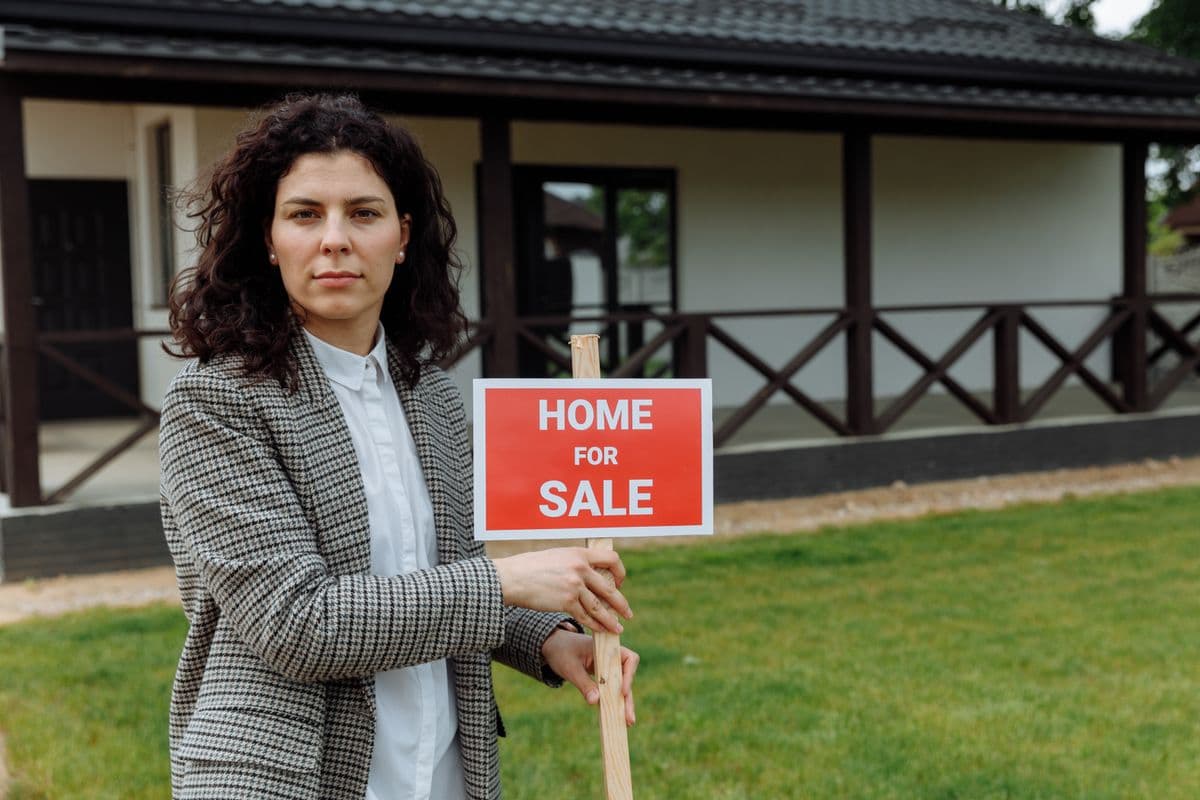 real estate agent standing outside a home with a for sale sign