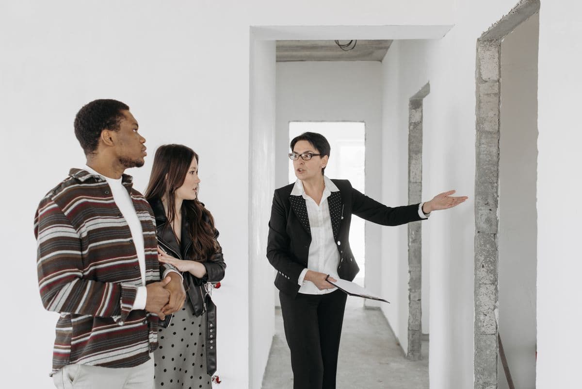 A woman with a clipboard guides two visitors through an unfinished home