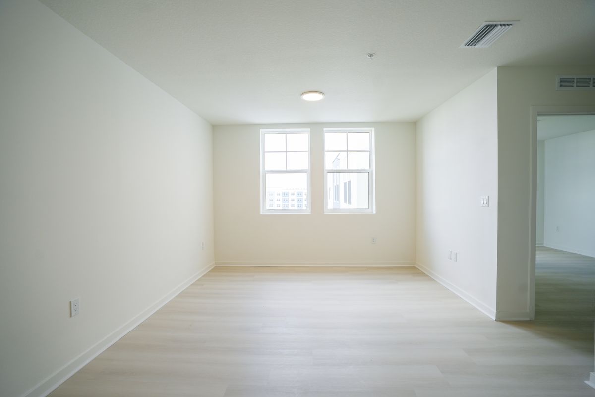 bright empty residential room with two windows and wood-look flooring
