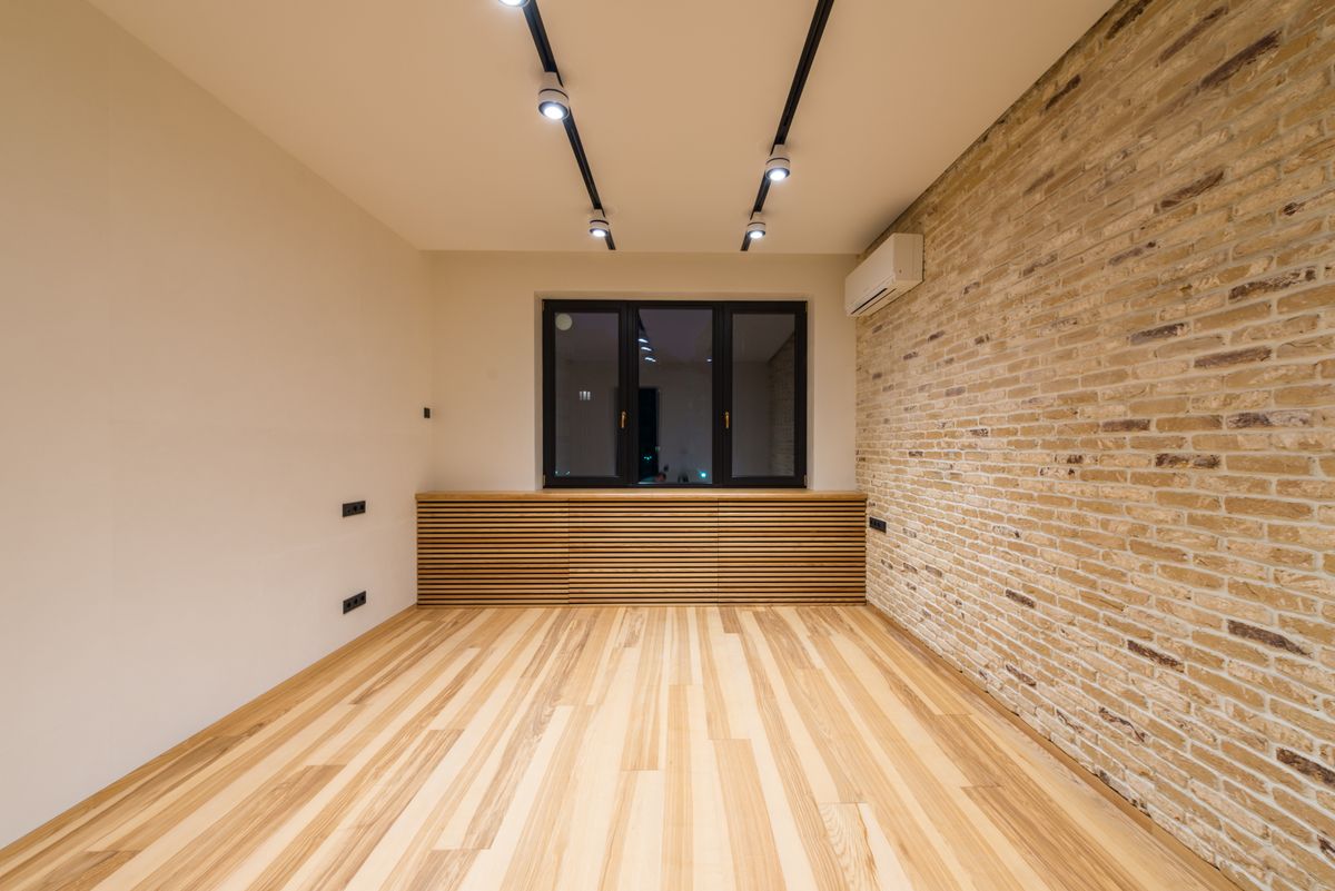 empty modern room with wood flooring, exposed brick, and a large window
