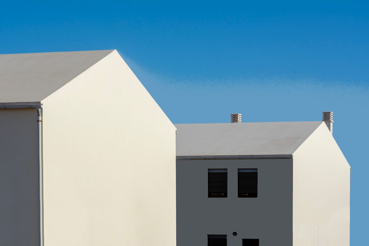 sunlit white modern home exterior with rooflines against a blue sky