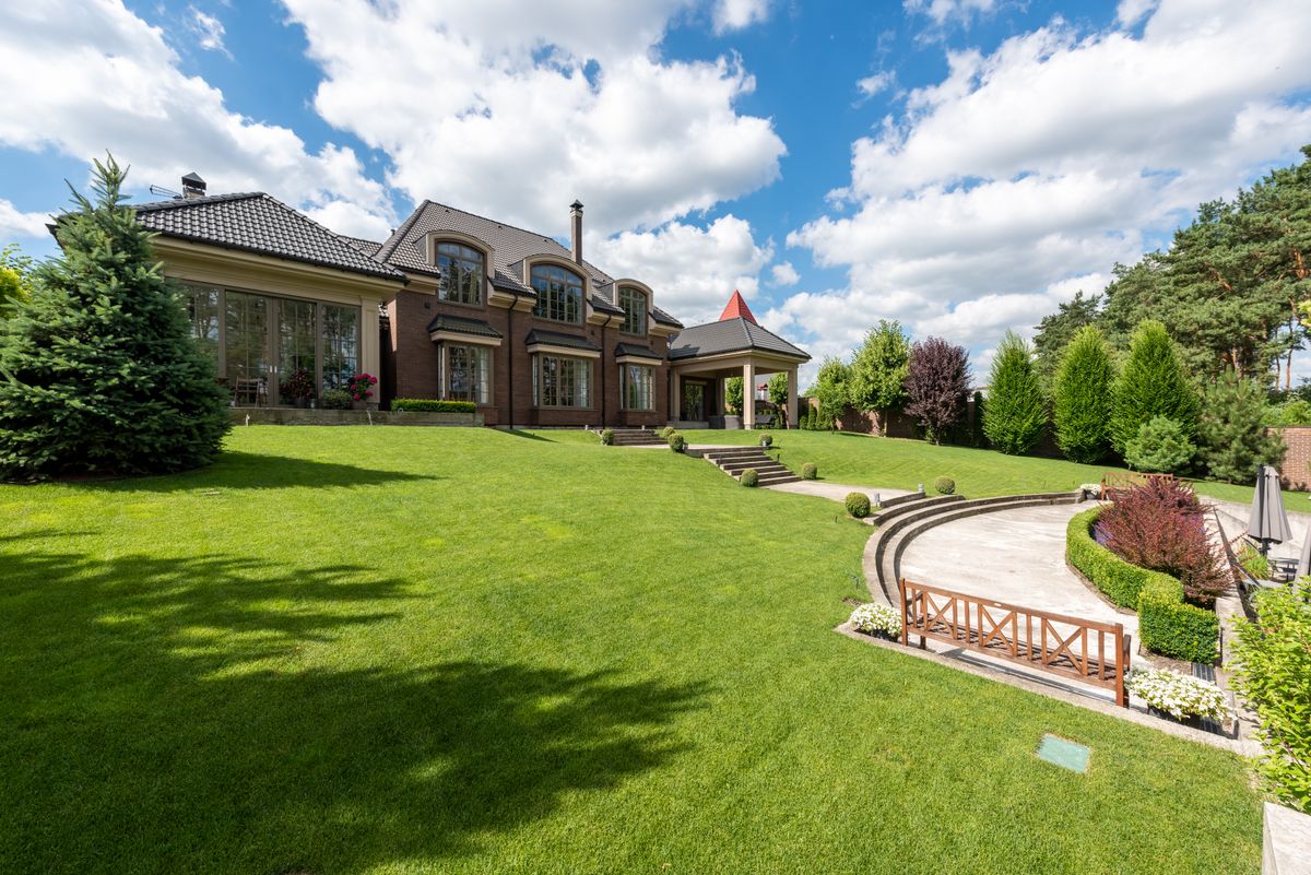 Large brick home overlooking a landscaped lawn, stone paths, and an outdoor patio